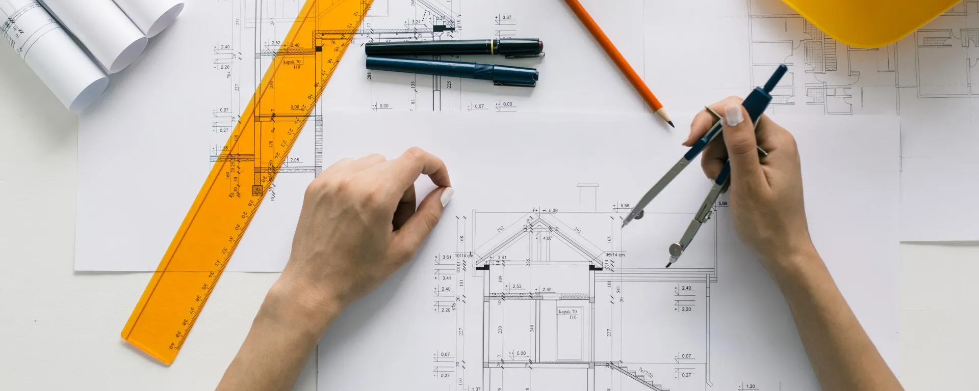 Una mujer sostiene un compás sobre el plano de una construcción. 