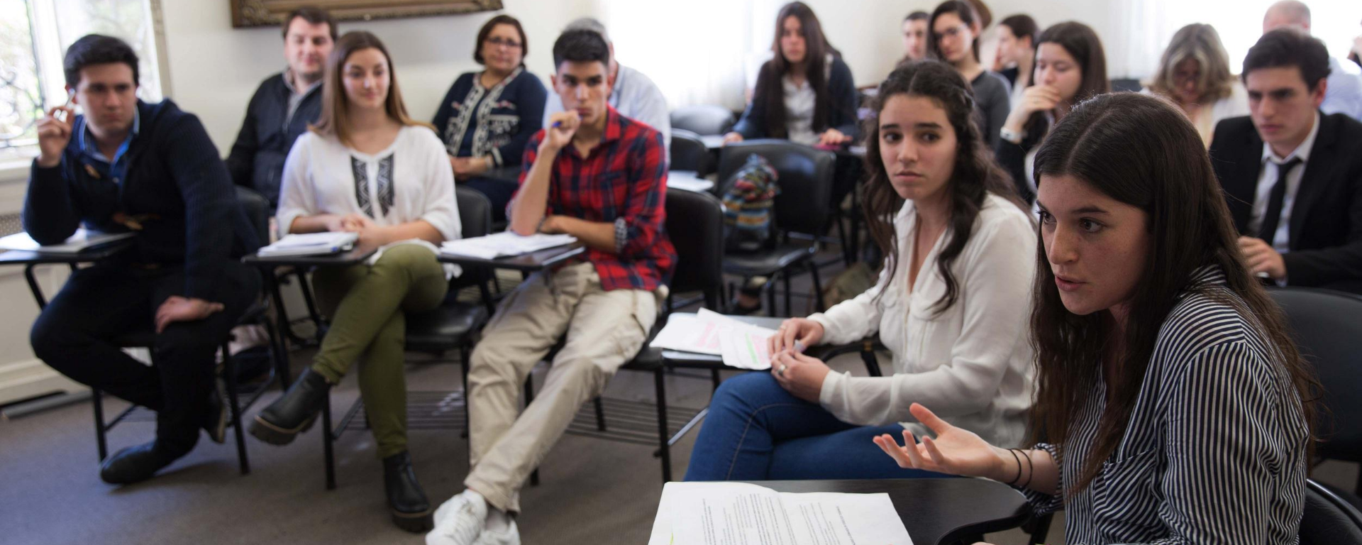 Una estudiante habla durante una clase. En el salón hay varios alumnos.