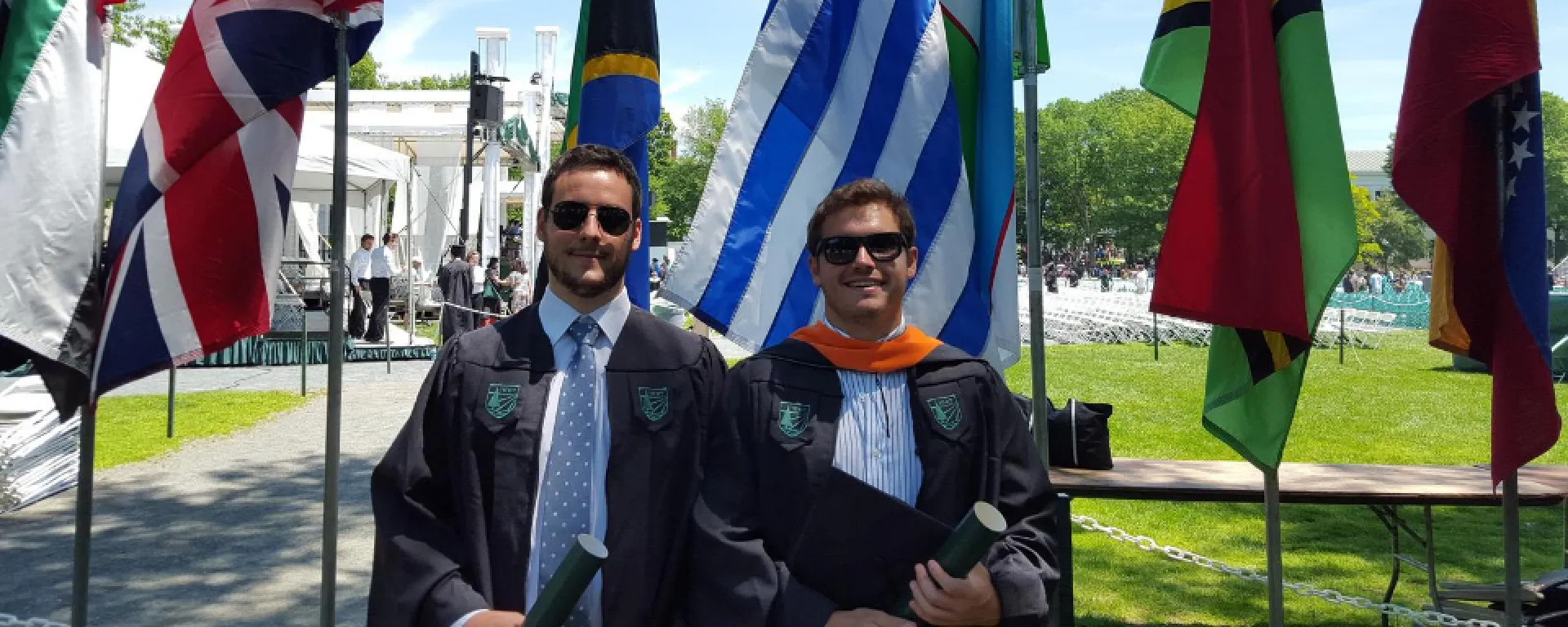 Santiago Haretche y Federico Mazzoli el día de su graduación en la Escuela de Negocios de Dartmouth. Santiago Haretche y Federico Mazzoli vestidos con toga. Detrás, la bandera uruguaya junto a otras banderas.