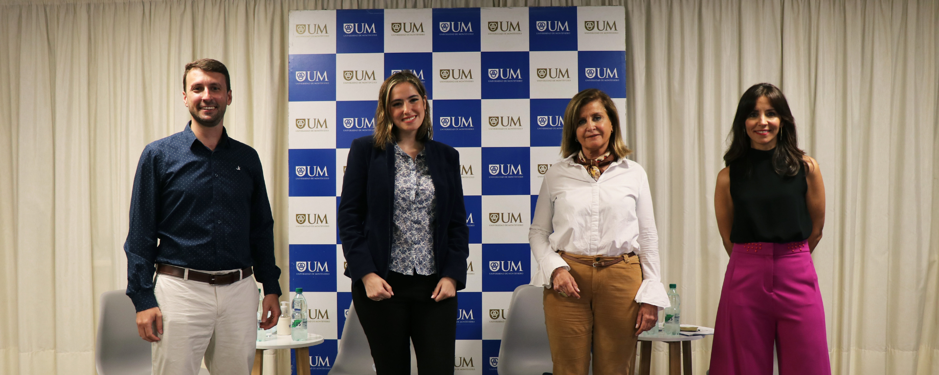 Un hombre y tres mujeres (panelistas del encuentro) miran a cámara. Se ecuentran en el salón de la actividad, detrás de ellos hay un panel con el logo de la UM.