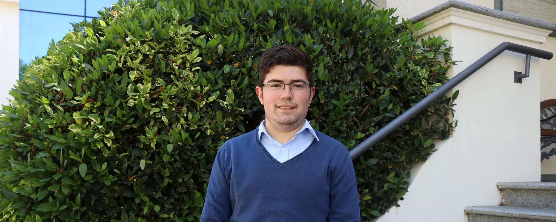 Mathias Loira ganó el Premio Academia Nacional de Economía de 2021. Estudiante universitario mira a cámara. Detrás se ve parte de una escalera y un arbusto.