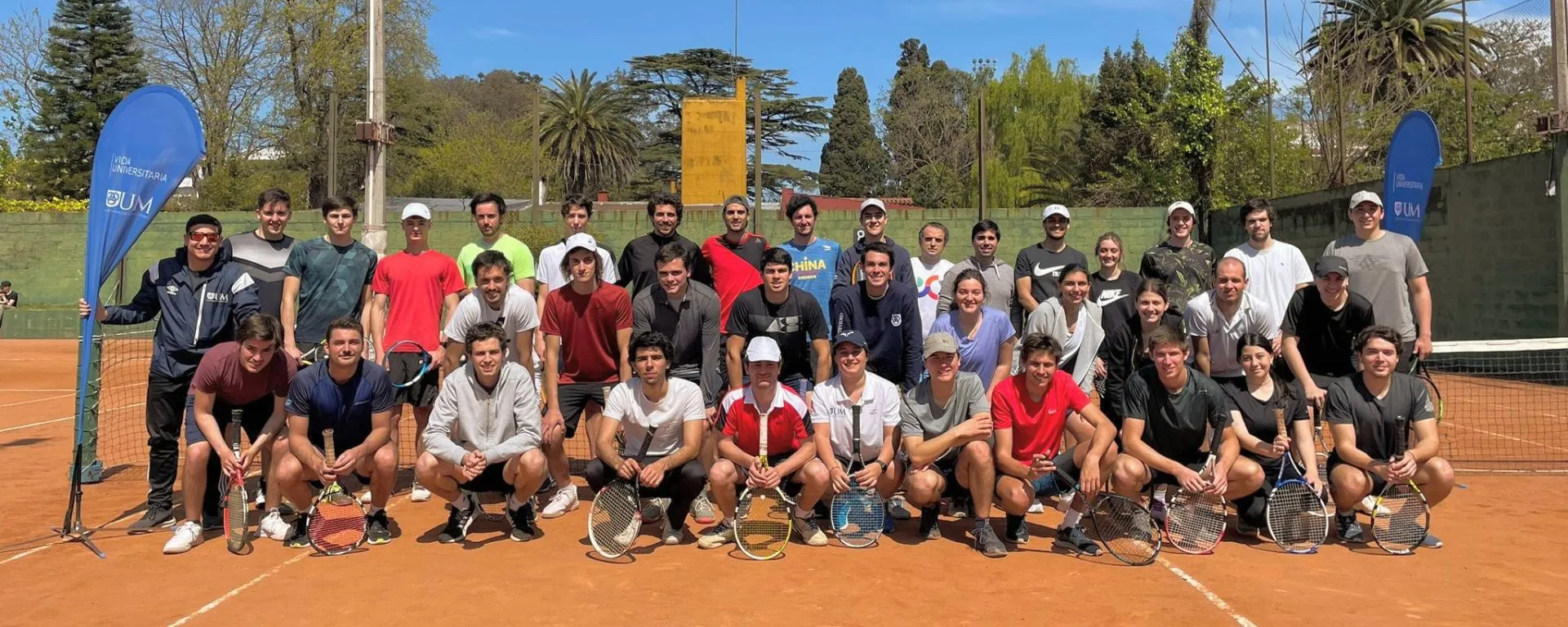 Portada de la noticia Torneo de tenis UM 2022 Torneo de tenis UM 2022, posan frente a cancha 42 participantes con raquetas al sol