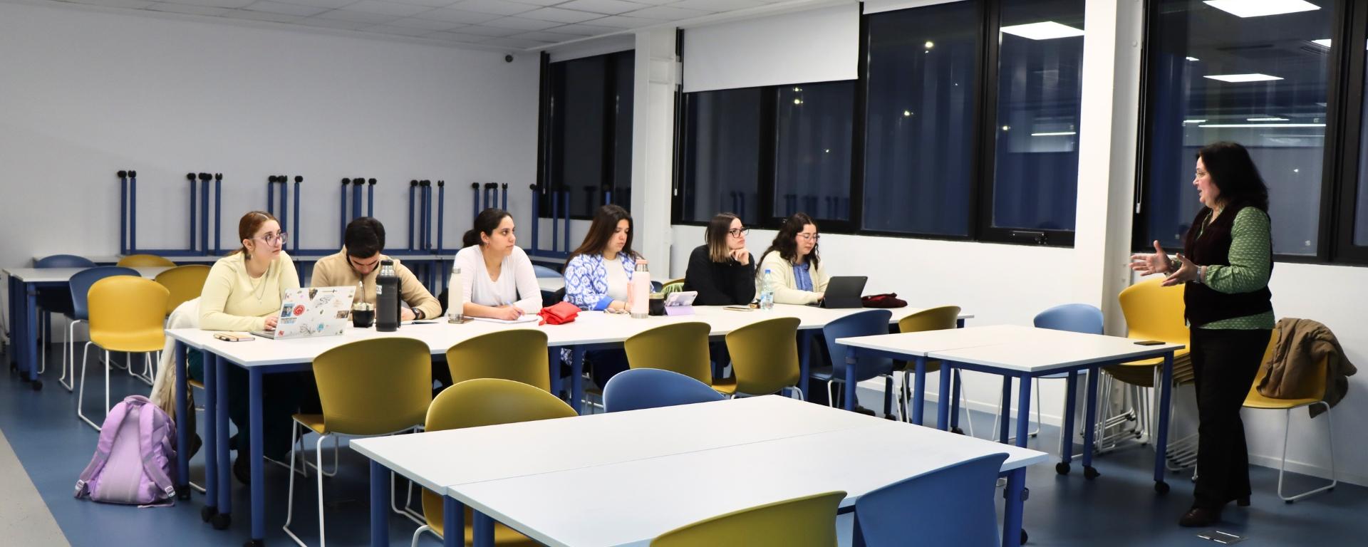 Estudiantes están en un salón de clases y la docente les está dando una conferencia
